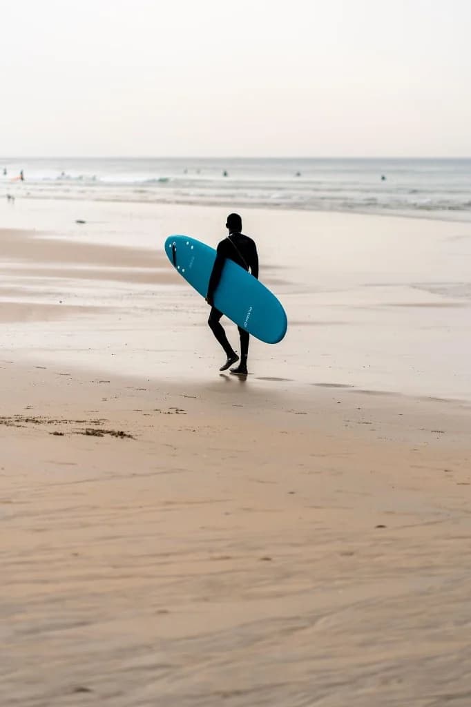Surfer walking on Taghazout beach with a blue board at dusk